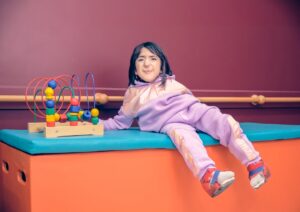 A parent and child sit together in a cozy living room, surrounded by soft lighting and sensory toys.