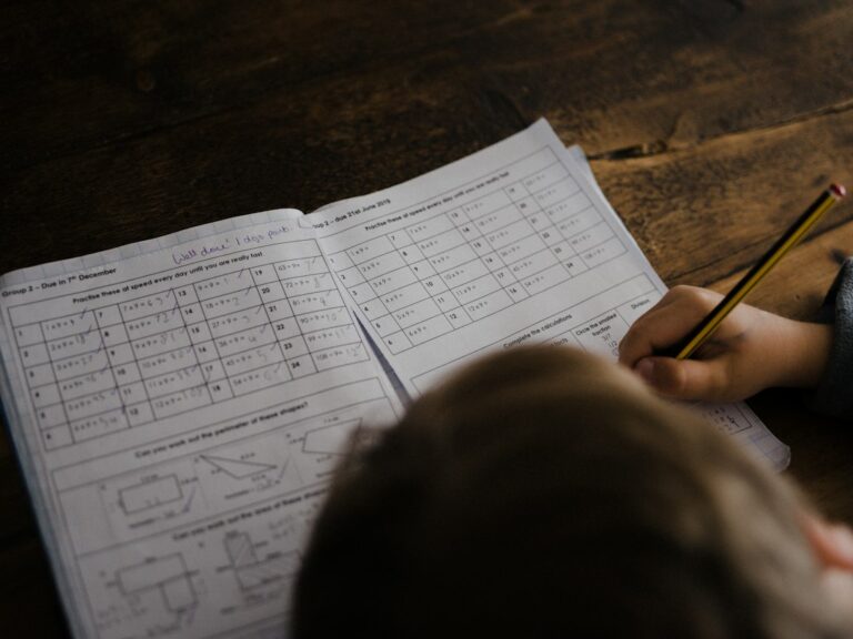 Student uses a checklist while organizing notebooks and completing homework at a kitchen table.