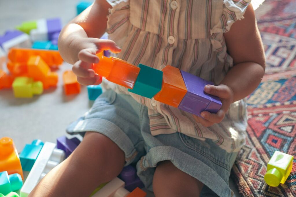 Child and caregiver build a colorful block structure on a living room floor.