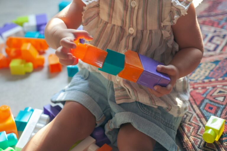 Child and caregiver build a colorful block structure on a living room floor.
